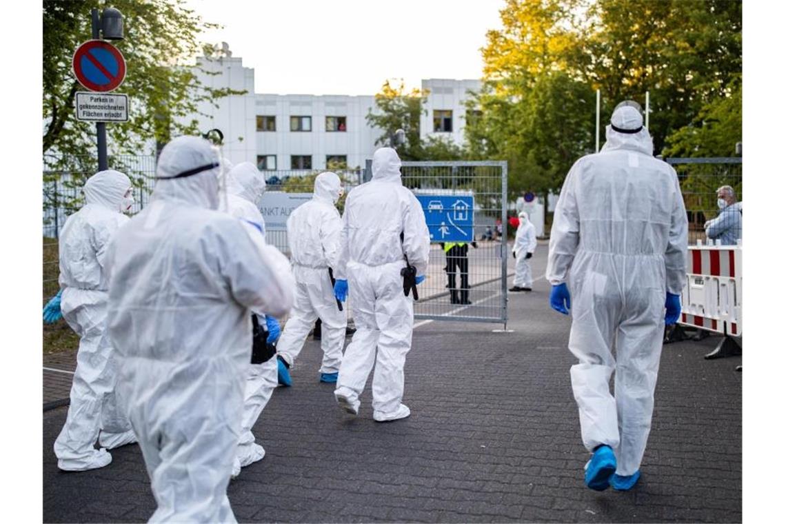 Beamte der Polizei und des Ordnungsamtes betreten in Schutzanzügen die Flüchtlingsunterkunft in St. Augustin. Foto: Marcel Kusch/dpa