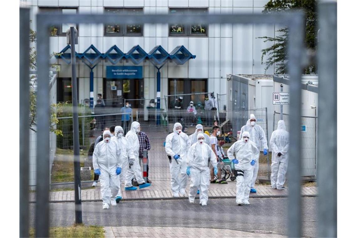 Beamte der Polizei und des Ordnungsamtes in Schutzanzügen vor der St. Augustiner Flüchtlingsunterkunft in NRW. Foto: Marcel Kusch/dpa