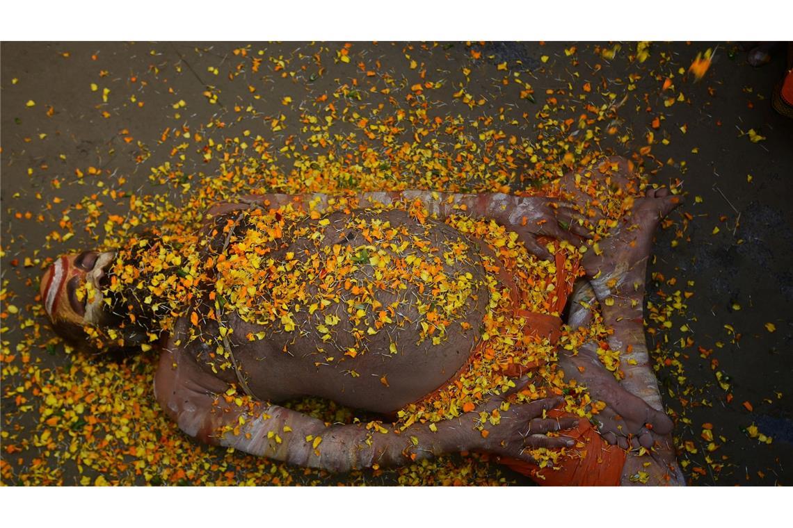 Bei einem hinduistischen Frühlingsfest in Indien liegt ein Sadhu mit Blütenblättern bedeckt auf der Straße.