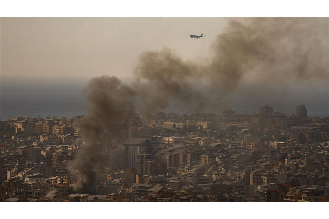 Beirut, Libanon: Verkehrsflugzeug im Landeanflug, während Rauch nach israelischen Luftangriffen aus südlichem Vorort aufsteigt