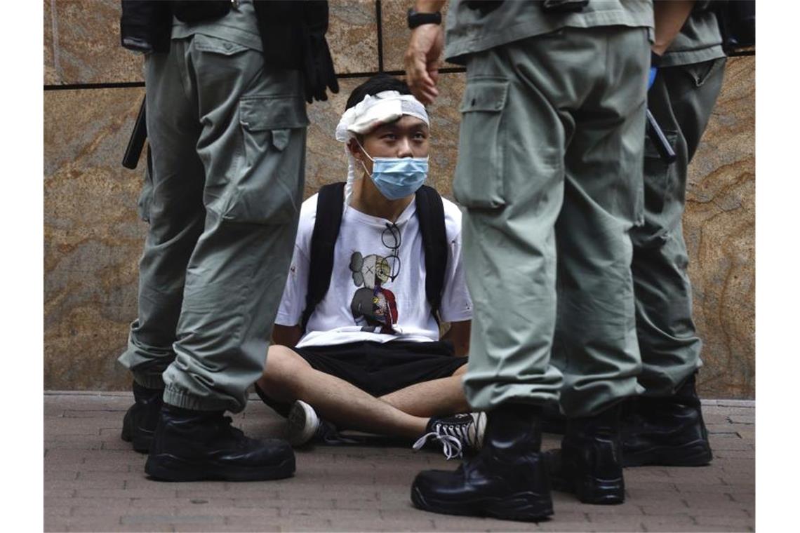 Bereitschaftspolizisten stehen im Hongkonger Central District um einen auf dem Boden sitzenden Demonstranten. Foto: Kin Cheung/AP/dpa