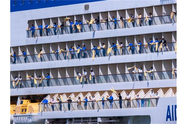 Besatzungsmitglieder winken mit Handtüchern von den Balkons eines Aida-Kreuzfahrtschiffs, das in den Hafen von Rostock einläuft. Foto: Jens Büttner/dpa-Zentralbild/dpa