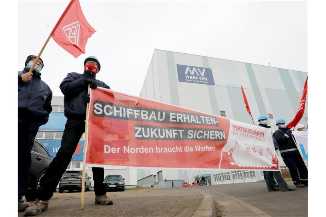 Wie geht es weiter bei den MV-Werften? Beschäftigte der Werft stehen mit Fahnen und Transparenten vor der Schiffbauhalle in Wismar. Foto: Bernd Wüstneck/dpa-Zentralbild/dpa