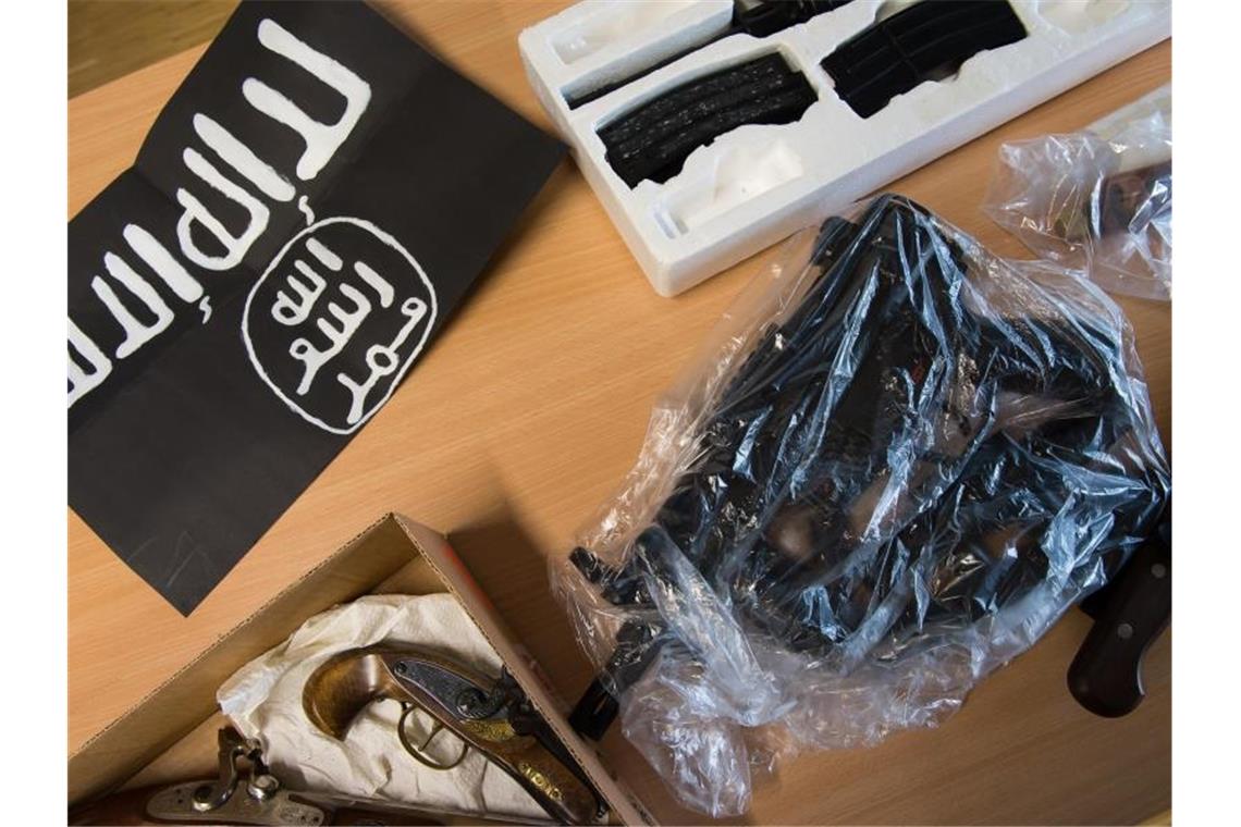 Beschlagnahmte Gegenstände liegen während einer Pressekonferenz der Polizei neben einer IS-Flagge. Foto: Swen Pförtner/dpa