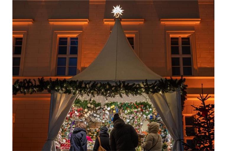 Besucher eines Weihnachtsmarktes stehen an einem Verkaufsstand für Christbaumschmuck. Foto: Moritz Frankenberg/dpa/Symbolbild