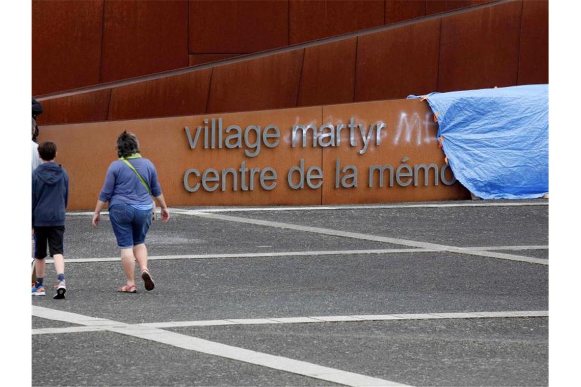 Besucher gehen an einem abgedeckten Graffiti auf dem Schriftzug am Eingang der Gedenkstätte in Oradour-sur-Glane vorbei. Unbekannte hatten unter anderem das Wort „Märtyrer“ im Schriftzug mit weißer Farbe durchgestrichen und „Lügner“ daneben geschrieben. Foto: Pascal Lachenaud/AFP/dpa