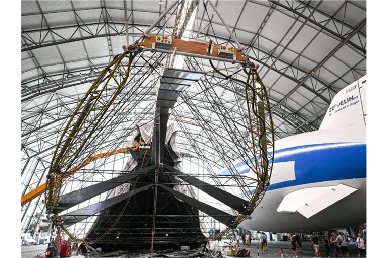 Besucher schauen sich den im Wiederaufbau befindlichen Zeppelin NT an, über den derzeit die Hülle gestülpt wird. Foto: Felix Kästle