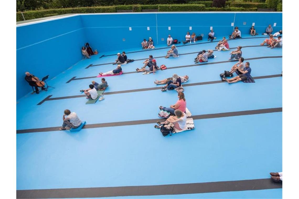 Klassik statt Kraulen: Freibadbecken wird zum Konzertsaal Besucher sehen sich im leeren Schwimmbecken ein Cello-Konzert. Foto: Christoph Schmidt/dpa