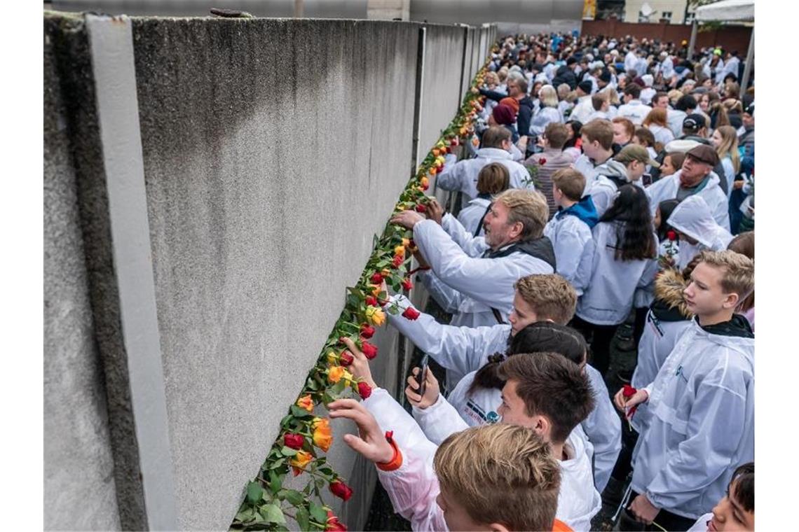 Rosen, Kerzen und Danke an die Nachbarn - 30 Jahre Mauerfall Besucher stecken Blumen bei der Gedenkveranstaltung der Stiftung Berliner Mauer an der Bernauer Straße in Mauerschlitze der Hinterlandmauer. Foto: Michael Kappeler/dpa