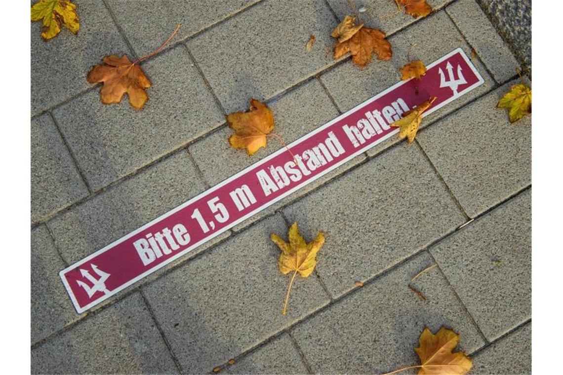 Blätter liegen neben einem Aufkleber mit der Aufschrift, „Bitte 1,5 m Abstand halten“ auf dem Boden. Foto: Gregor Fischer/dpa/Symbolbild
