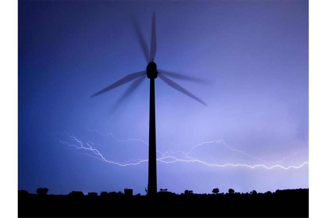Blitze zucken am Horizont hinter einem Windrad. Foto: Julian Stratenschulte/Archivbild