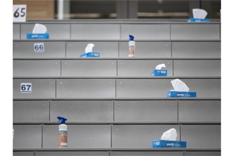 Boxen mit Papiertüchern und Sprühflaschen mit Desinfektionsmittel stehen in einem Hörsaal. Foto: Sebastian Gollnow/dpa/Archivbild