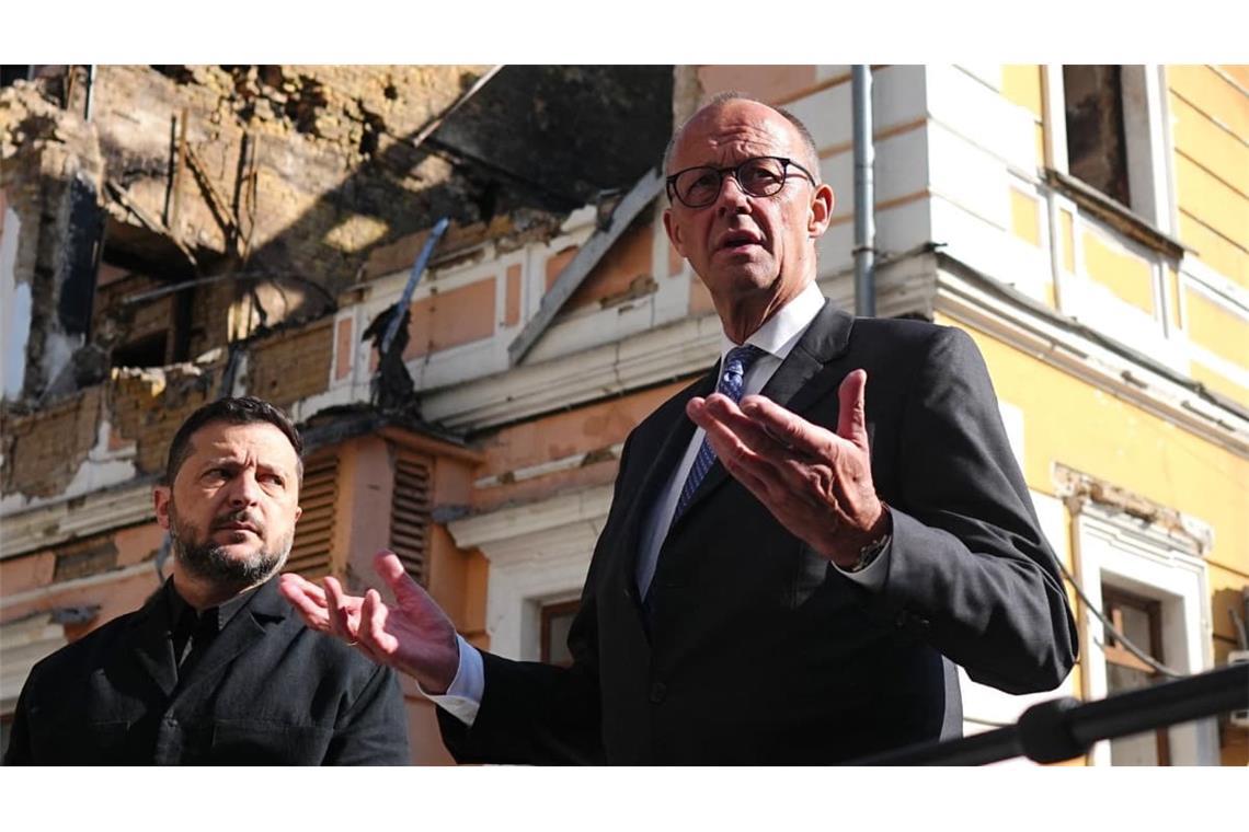 Bundeskanzler Friedrich Merz (r, CDU) und der ukrainische Präsident Wolodymyr Selenskyj (l) vor dem zerstörten Gebäude der Nationalen Akademie der Wissenschaften in Kiew. Es wurde im September bei einem russischen Angriff zerstört.