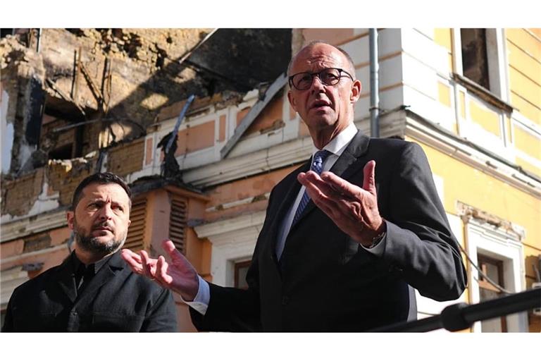 Bundeskanzler Friedrich Merz (r, CDU) und der ukrainische Präsident Wolodymyr Selenskyj (l) vor dem zerstörten Gebäude der Nationalen Akademie der Wissenschaften in Kiew. Es wurde im September bei einem russischen Angriff zerstört.