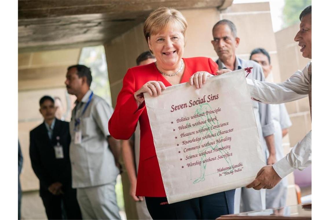 Bundeskanzlerin Angela Merkel bekommt nach einer Gedenkzeremonie für Mahatma Gandhi ein Banner mit den „Seven Social Sins“. Foto: Michael Kappeler/dpa