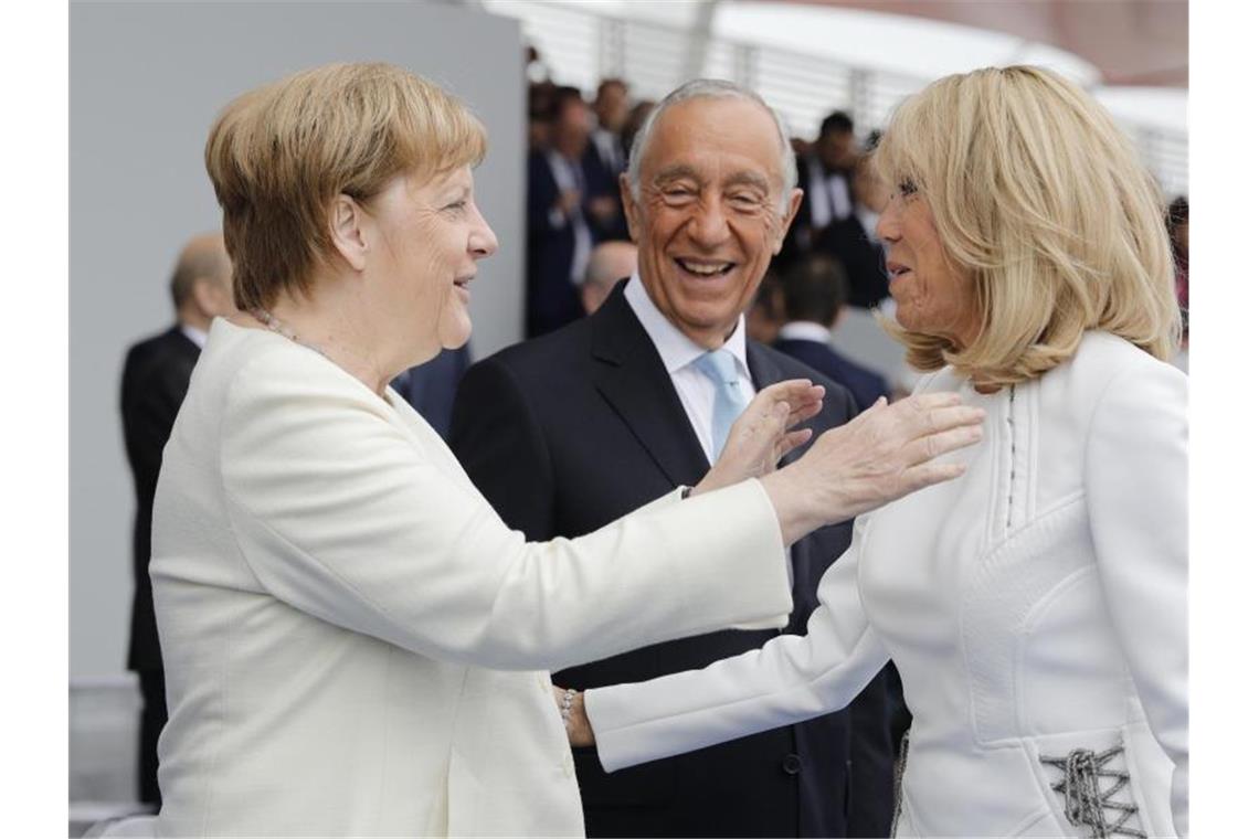 Bundeskanzlerin Angela Merkel (l) und Brigitte Macron begrüßen sich. Viele europäische Staats- und Regierungschefs verfolgen auf der Ehrentribüne die Militärparade. Foto: Kamil Zihnioglu/AP