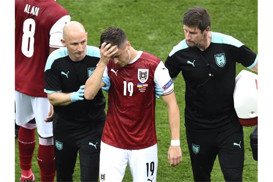 Dank Baumgartner: Österreich erstmals im EM-Achtelfinale Christoph Baumgartner (M) aus Österreich wird nach einer Verletzung von medizinischen Mitarbeitern vom Spielfeld geführt. Foto: Mihai Barbu/Pool AFP/AP/dpa