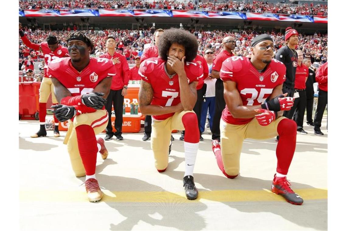 Colin Kaepernick (M.) kniete 2016 mit seinen Teamkollegen Eli Harold (l) und Eric Reid vor einem Spiel der San Francisco 49ers. Foto: John G Mabanglo/EPA/dpa