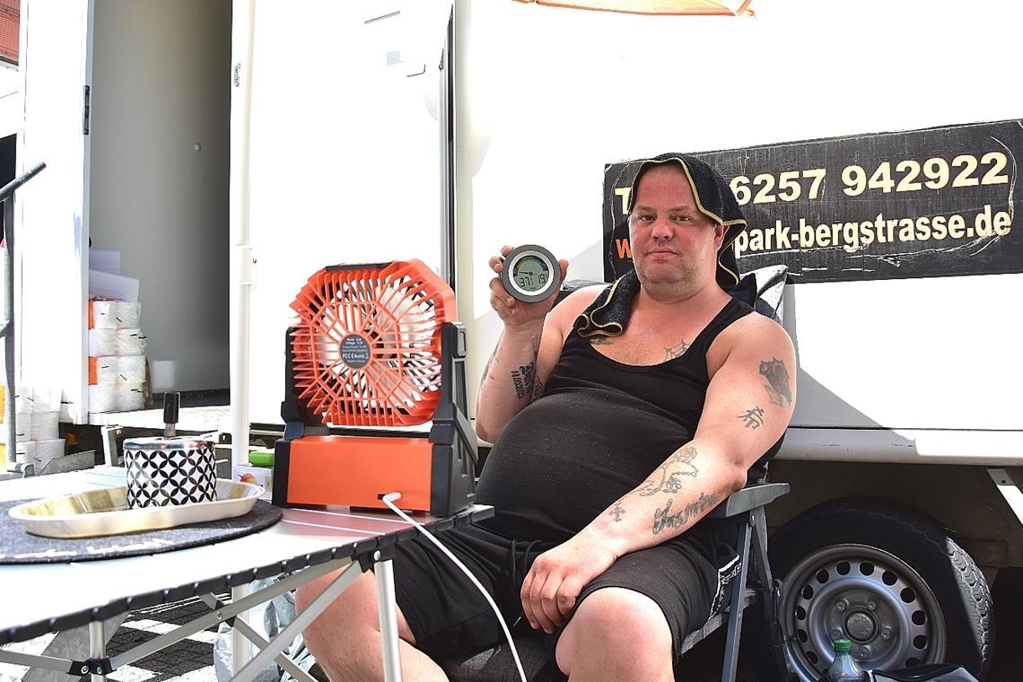 Daniel Jost sorgt am Toilettenwagen in der Marktstraße für Ordnung. Mit einem Ventilator, einem Sonnenschirm und einem nassen Handtuch auf dem Kopf verschafft er sich etwas Abkühlung.