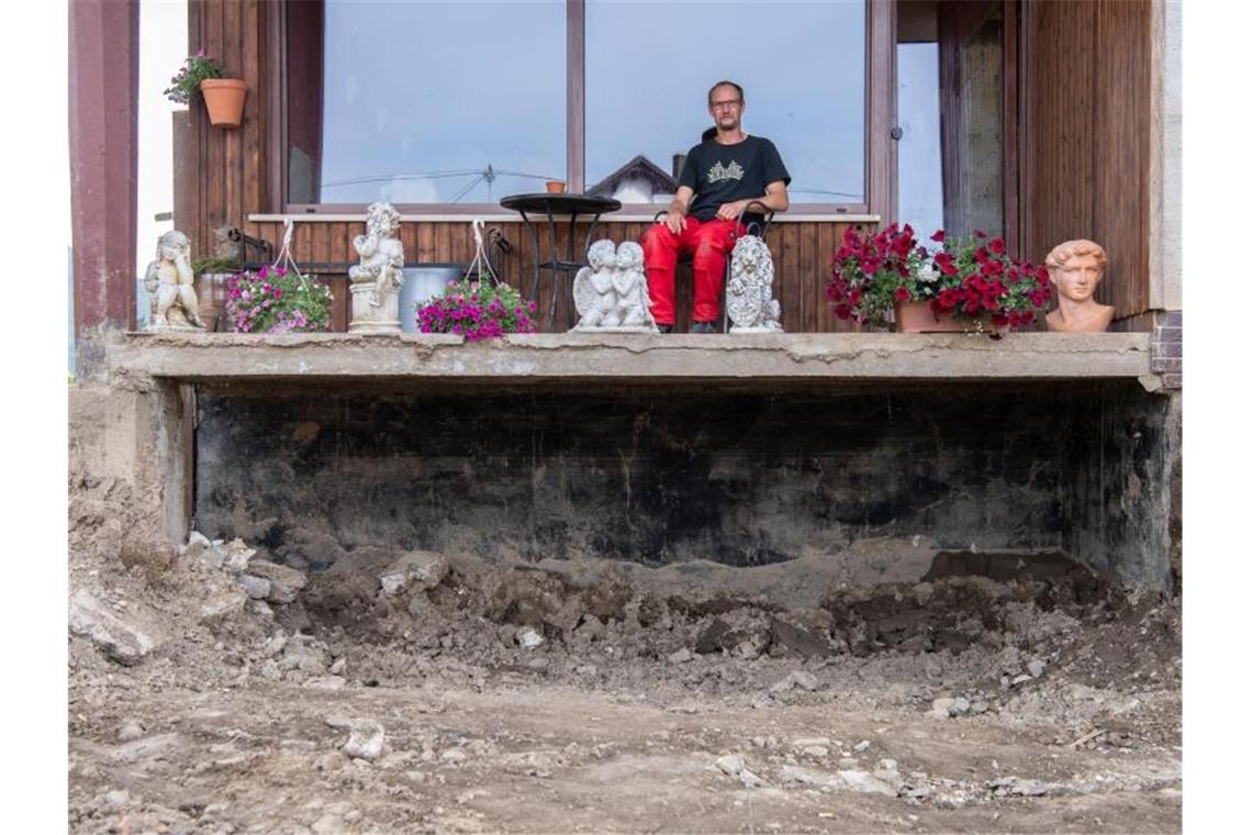 Aufbauen oder gehen? - Zwei Wochen nach der Flut im Ahrtal Daniel Schmitz sitzt auf dem Balkon seiner durch die Flut zerstörten Wohnung. Vom einst liebevoll gestalteten Garten ist nichts mehr übrig geblieben. Foto: Boris Roessler/dpa