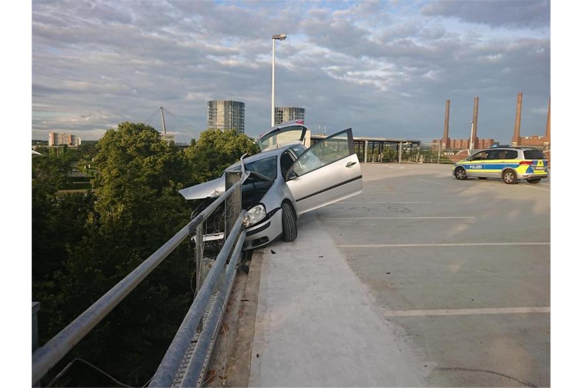 Das Auto hängt in der Sicherungsplanke auf einem Parkhausdeck in Wolfsburg. Foto: -/Polizei Wolfsburg/dpa