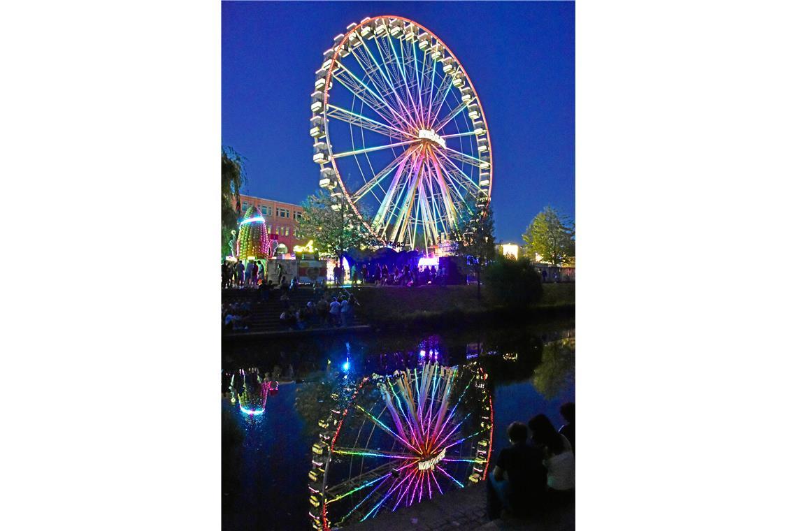 Das bunt beleuchtete Riesenrad spiegelt sich in der Murr.