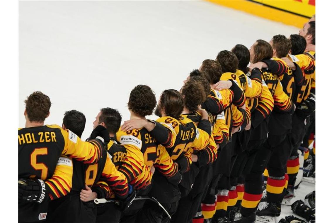 Das deutsche Eishockey-Nationalteam steht Arm in Arm auf dem Eis. Foto: Roman Koksarov/dpa