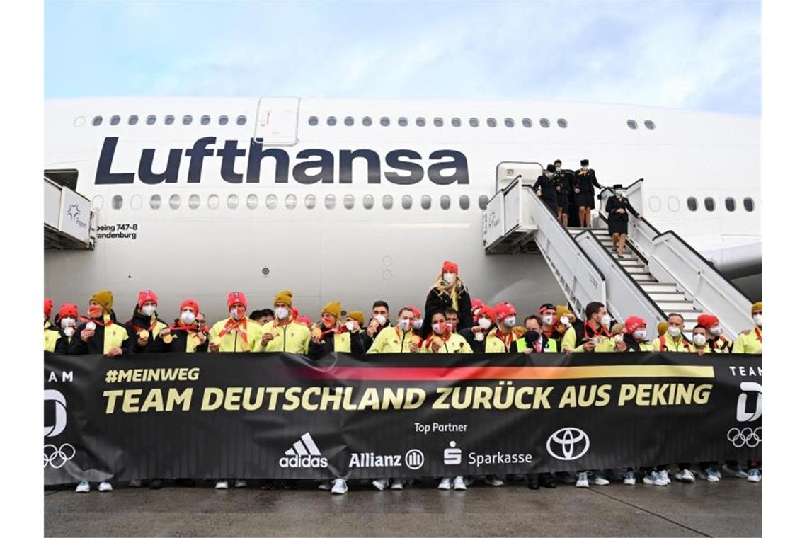 Mit Medaillenposen: Weitere Sportler zurück aus Peking Das deutsche Olympia-Team steht bei der Rückkehr von den Winterspielen auf dem Frankfurter Flughafen hinter einem Plakat: „Team Deutschland zurück aus Peking“. Foto: Arne Dedert/dpa