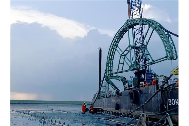 Das Endstück eines 516 Kilometer langen Seekabels für Strom wird von dem Kabelverlegeschiff „Boka Connector“ im Watt unter dem Deich hindurch an Land gezogen. Mit einer „Stromautobahn“ unter Wasser wollen Deutschland und Großbritannien einfacher Elektrizität handeln und austauschen. Foto: Carsten Rehder/dpa