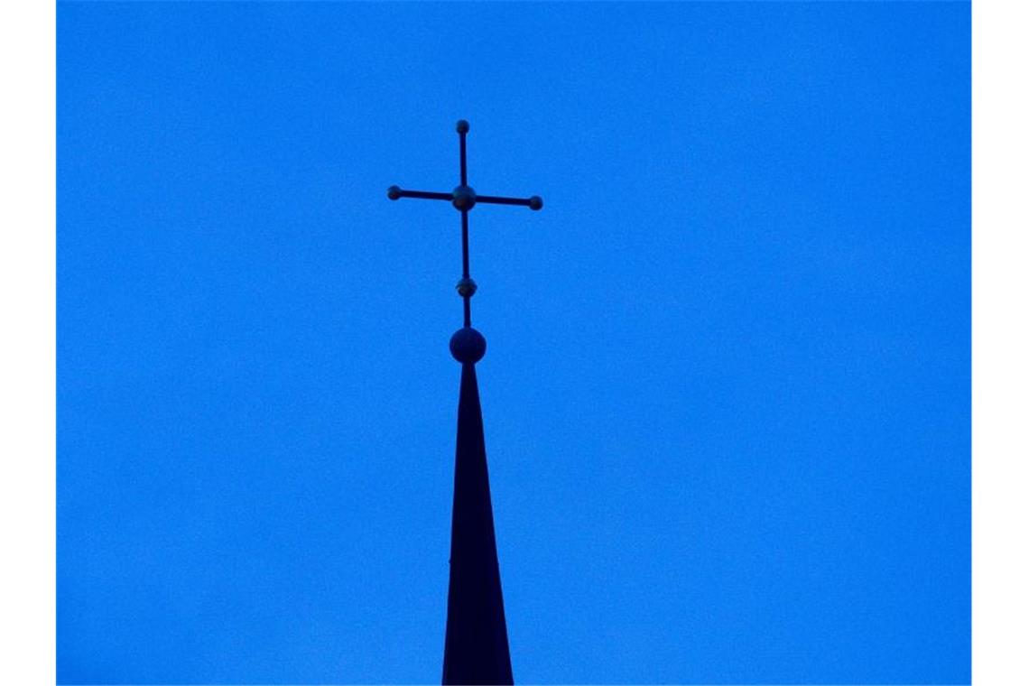 Das Kreuz einer evangelischen Kirche ist in der Abenddämmerung zu sehen. Foto: Friso Gentsch/Archivbild