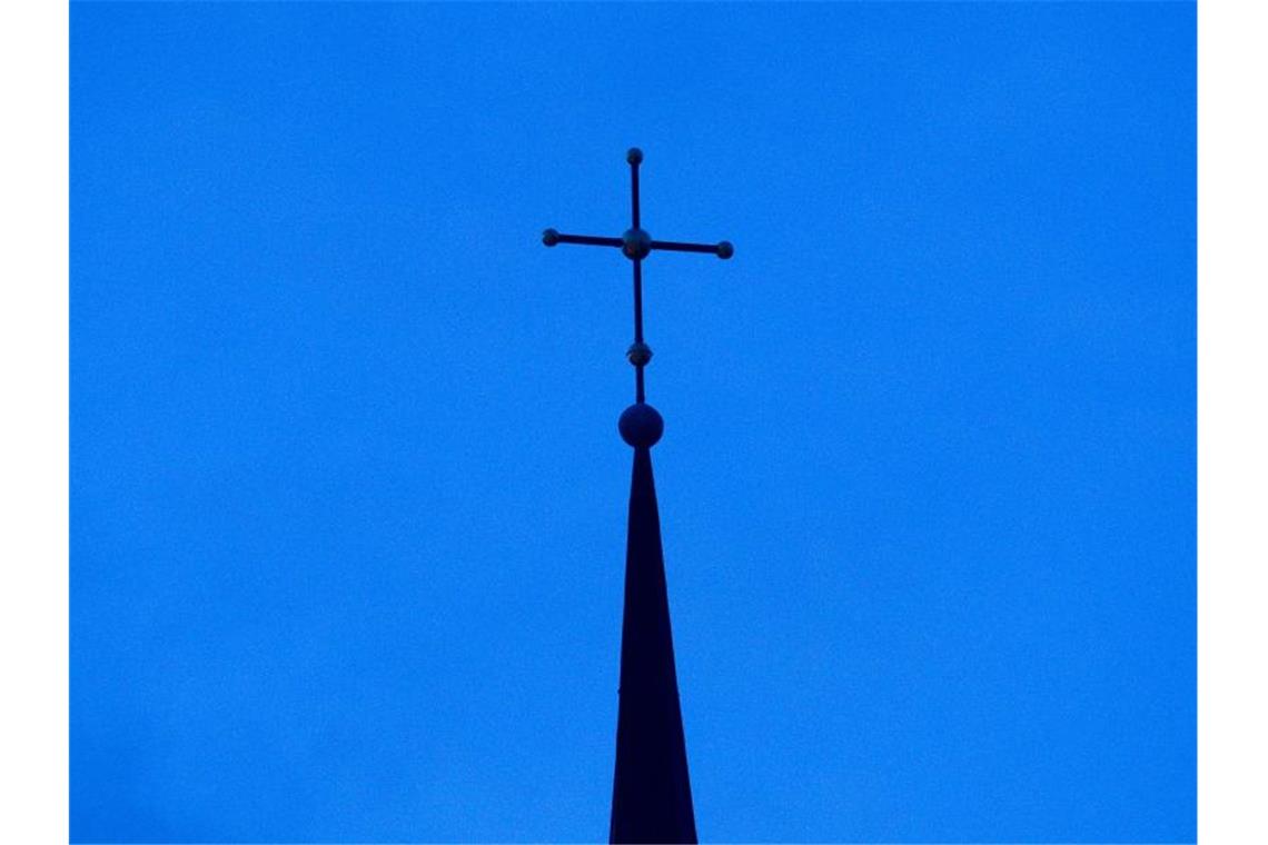 Das Kreuz einer Kirche ist auf einem Kirchendach zu sehen. Foto: Friso Gentsch/dpa/Archivbild