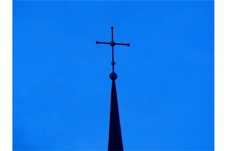 Das Kreuz einer Kirche ist in der Abenddämmerung zu sehen. Foto: Friso Gentsch/dpa/Symbolbild