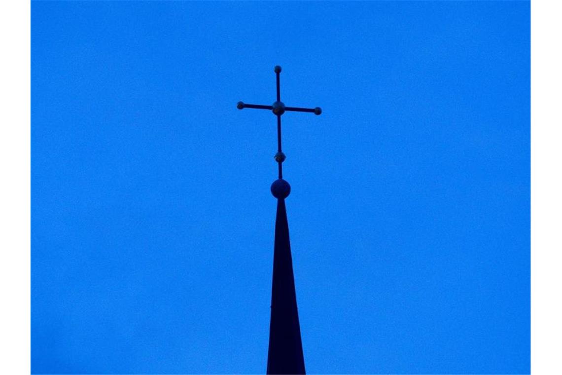 Das Kreuz einer Kirche ist in der Abenddämmerung zu sehen. Foto: Friso Gentsch/dpa/Symbolbild