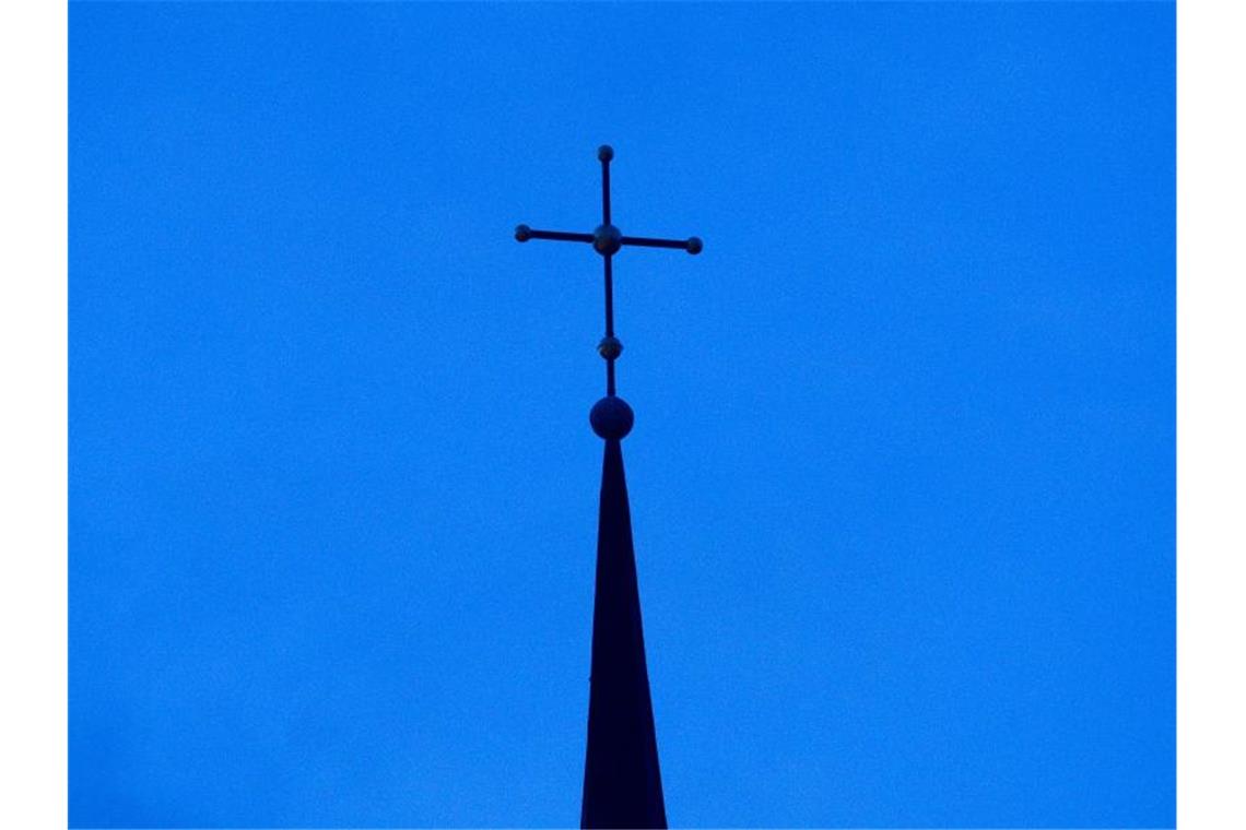 Priester sollen nur noch an wenigen Unis ausgebildet werden Das Kreuz einer Kirche ist in der Abenddämmerung zu sehen. Foto: Friso Gentsch/dpa/Symbolbild