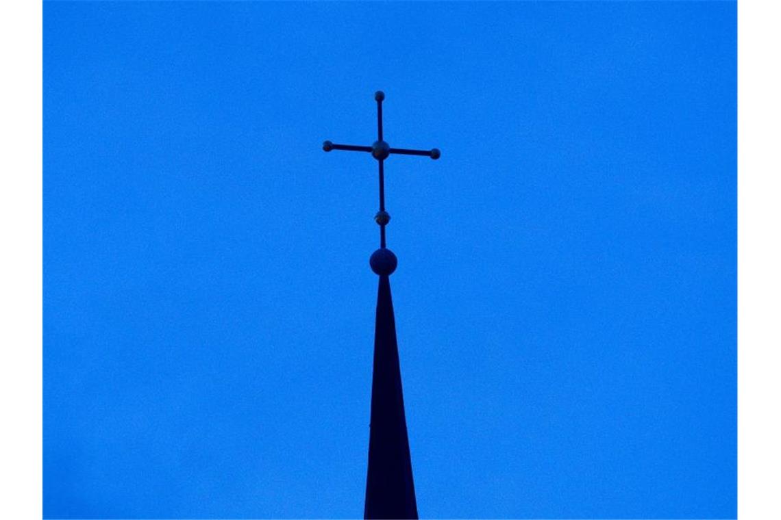 Das Kreuz einer Kirche ist in der Abenddämmerung zu sehen. Foto: Friso Gentsch/dpa/Symbolbild