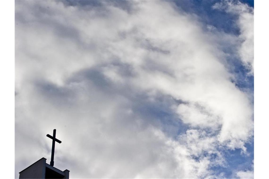 Das Kreuz einer Kirche ist vor bewölktem Himmel zu sehen. Foto: Nicolas Armer/dpa/Archivbild