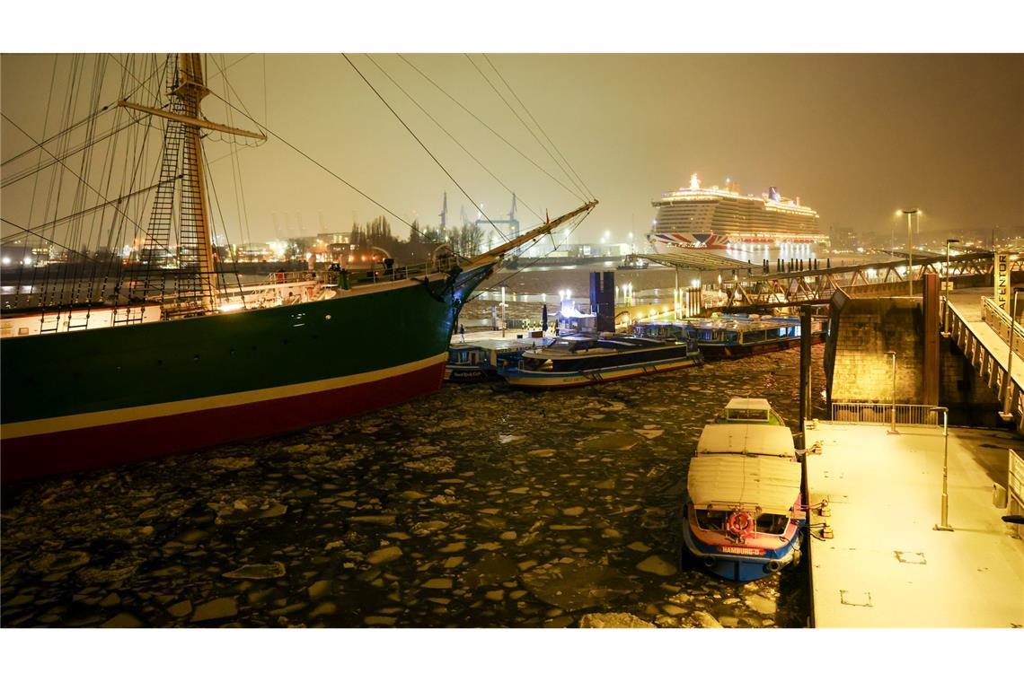 Das Kreuzfahrtschiff Iona (r) des britisch-amerikanischen Kreuzfahrtunternehmens P&O Cruises fährt an den Hamburger Landungsbrücken über die mit kleinen Eisschollen bedeckte Elbe in Richtung eines Kreuzfahrtterminals in der Hafencity.