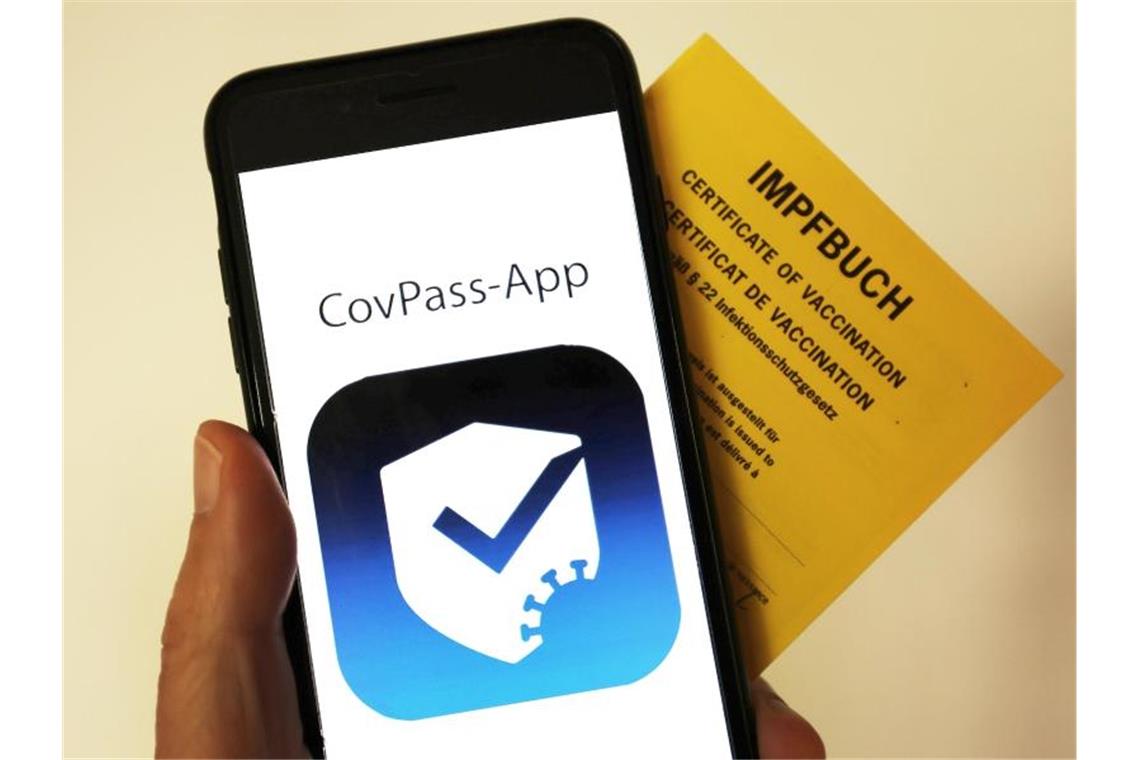 Das Logo der CovPass-App ist neben einem Impfbuch auf einem Smartphone zu sehen. Foto: Oliver Berg/dpa