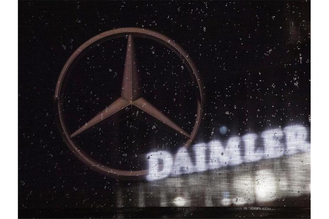 Das Logo der Daimler-AG ist an der Konzernzentrale zu sehen, im Vordergrund ist ein Mercedes-Stern auf einer Flagge abgebildet, die voller Regentropfen ist. Foto: Marijan Murat/dpa