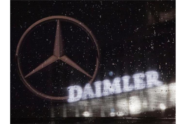 Das Logo der Daimler-AG ist an der Konzernzentrale zu sehen, im Vordergrund ist ein Mercedes-Stern auf einer Flagge abgebildet, die voller Regentropfen ist. Foto: Marijan Murat/dpa
