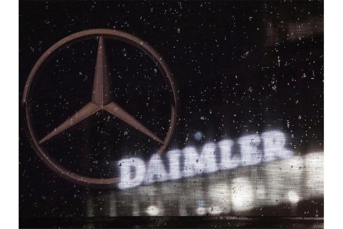 Das Logo der Daimler-AG ist an der Konzernzentrale zu sehen. Im Vordergrund ist ein Mercedes-Stern auf einer Flagge abgebildet, die voller Regentropfen ist. Foto: Marijan Murat/dpa/Archivbild
