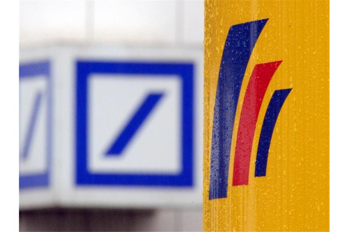 Das Logo einer Filiale der Deutschen Bank (l) und das Logo der auf der gegenüberliegenden Straßenseite befindlichen Postbank-Zentrale. Foto: Federico Gambarini/dpa