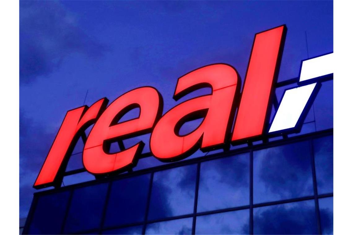 Das Real-Logo leuchtet am Morgen auf dem Dach eines Real Warenhauses in Köln. Foto: Oliver Berg/dpa