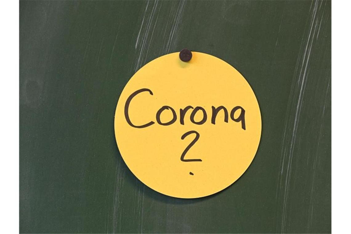 Das Wort "Corona?" ist auf einem kreisrunde Papierschilder geschrieben, das an der Tafel angebracht ist. Foto: Felix Kästle/dpa/Symbol