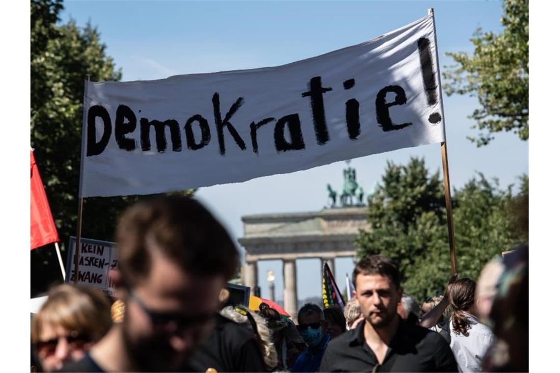 "Demokratie!" steht auf einem Banner, das von Teilnehmern auf der Demonstration gegen die Corona-Beschränkungen vor dem Brandenburger Tor Anfang August getragen wird. Foto: Paul Zinken/dpa-zentralbild/dpa