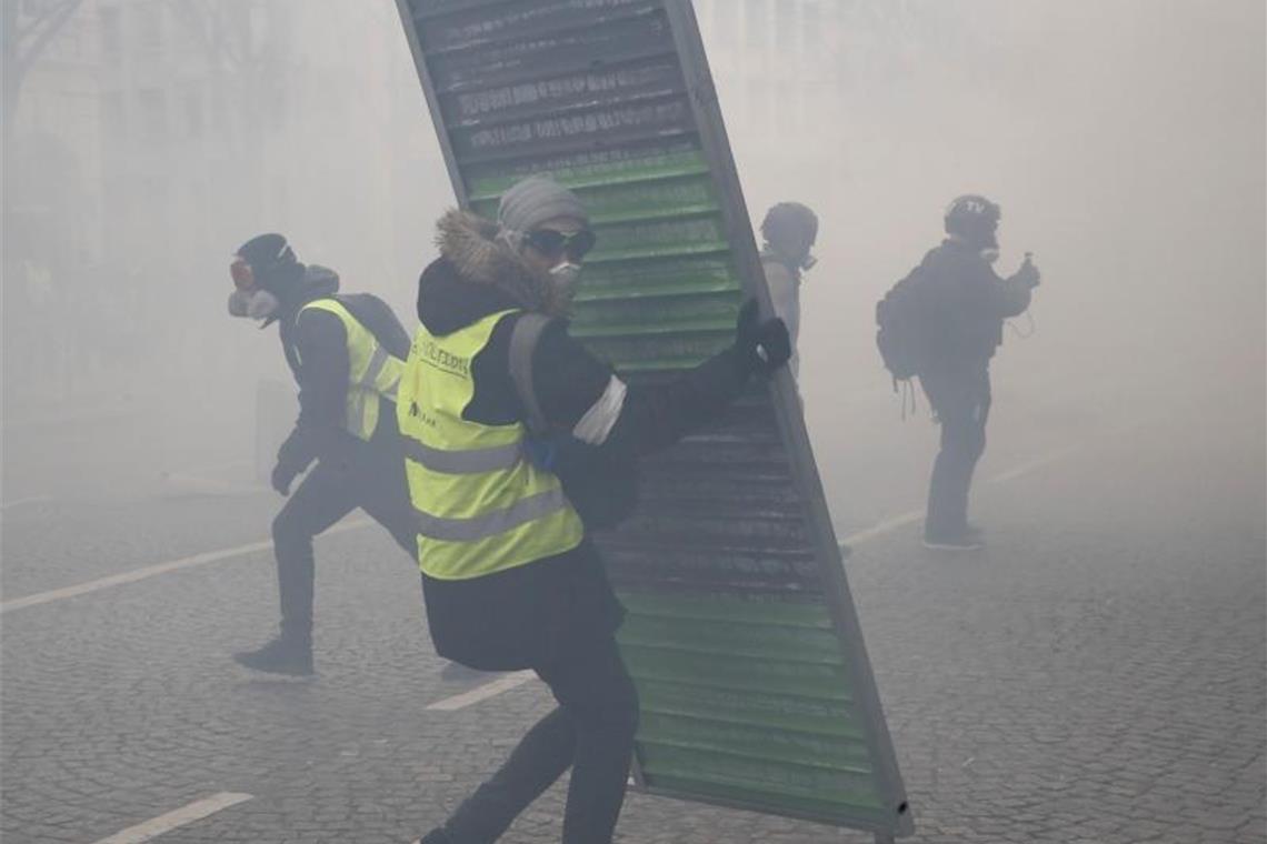 Demonstranten errichten Barrikaden im Tränengasnebel auf den Champs-Élysées. Foto: Christophe Ena/AP/dpa