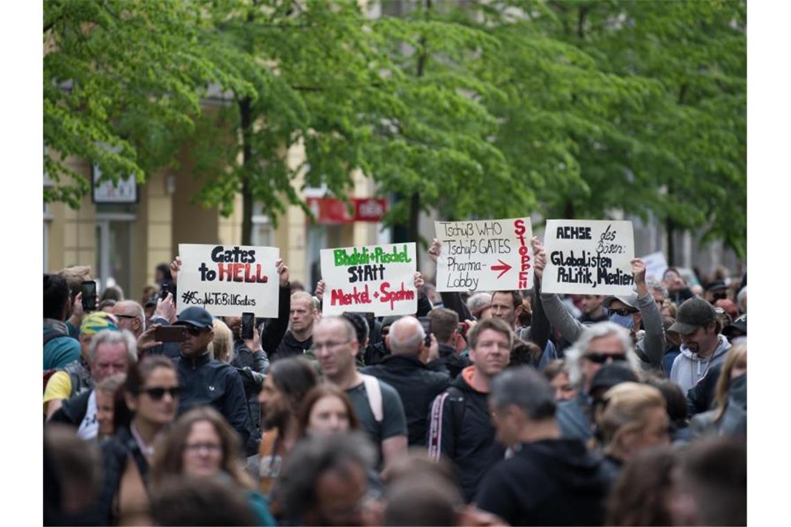 Demonstranten halten bei der Kungebung in Berlin Schilder hoch, auf denen sie unter anderem Bill Gates und die WHO angreifen. Foto: Jörg Carstensen/dpa