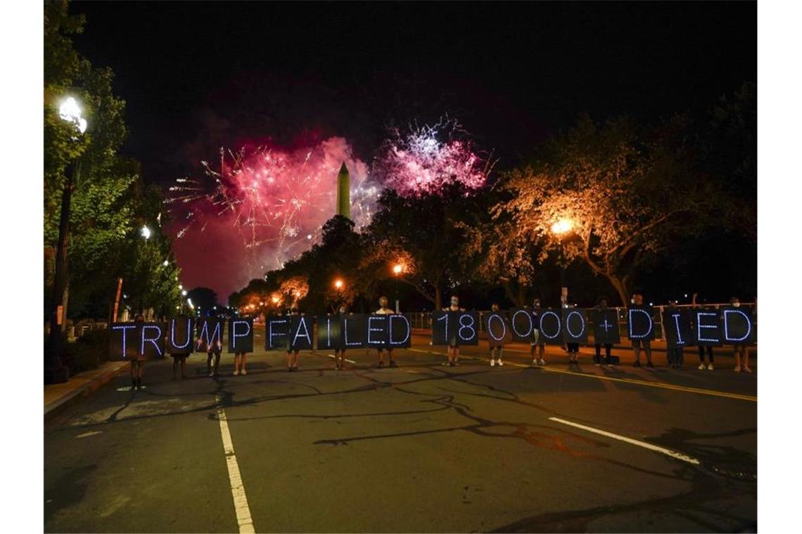 Demonstranten halten Schilder auf denen Leuchtdioden eine Botschaft bilden, während ein Feuerwerk den Himmel um das Washington Monument erhellt, welches zum Abschluss des Parteitages der Republikaner gezündet wird. Foto: Carolyn Kaster/AP/dpa