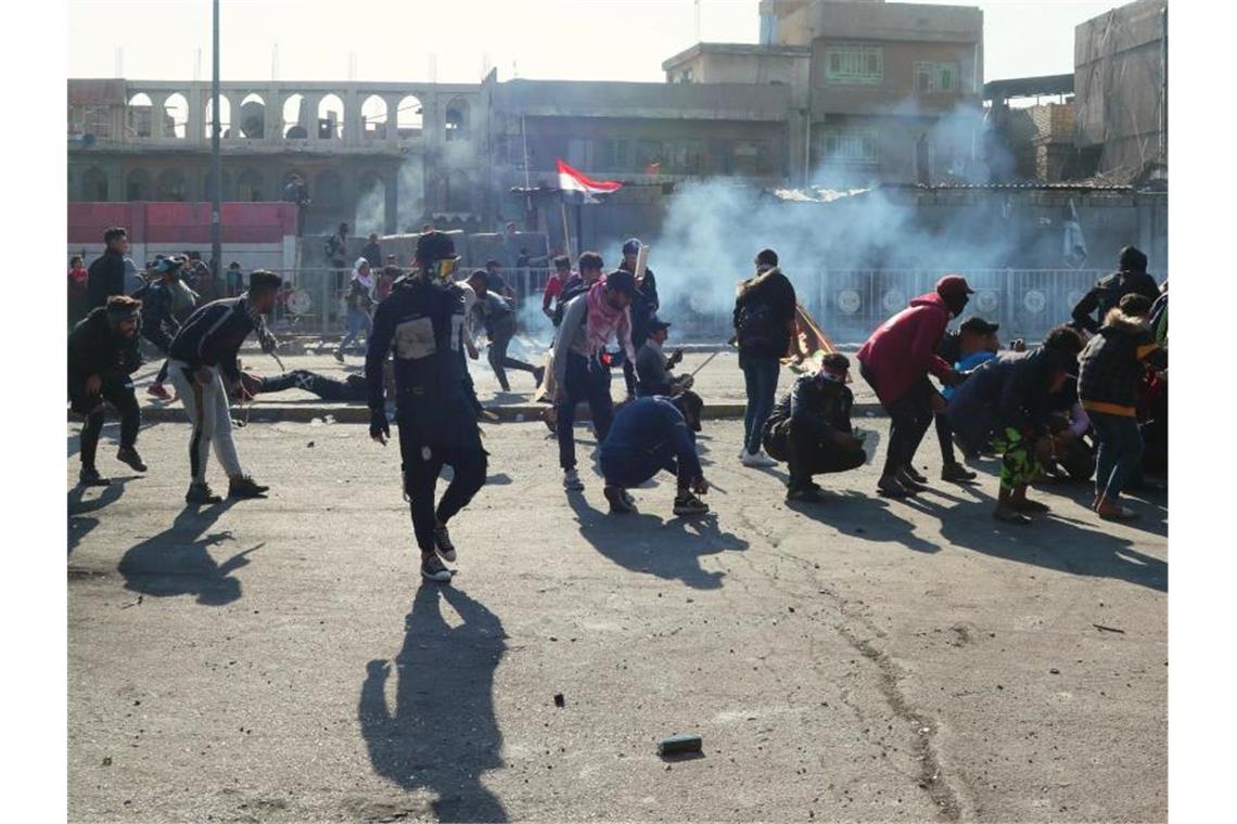 Demonstranten in Bagdad gehen vor Tränengasgeschossen in Deckung. Foto: Hadi Mizban/AP/dpa