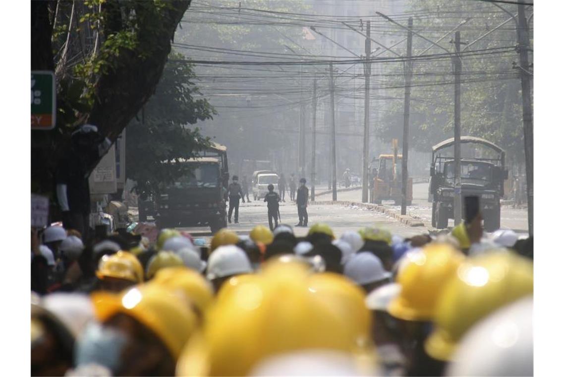 Demonstranten in Mandalay tragen gelbe Schutzhelme und beobachten auf einer blockierten Straße die Polizei. Foto: Uncredited/AP/dpa